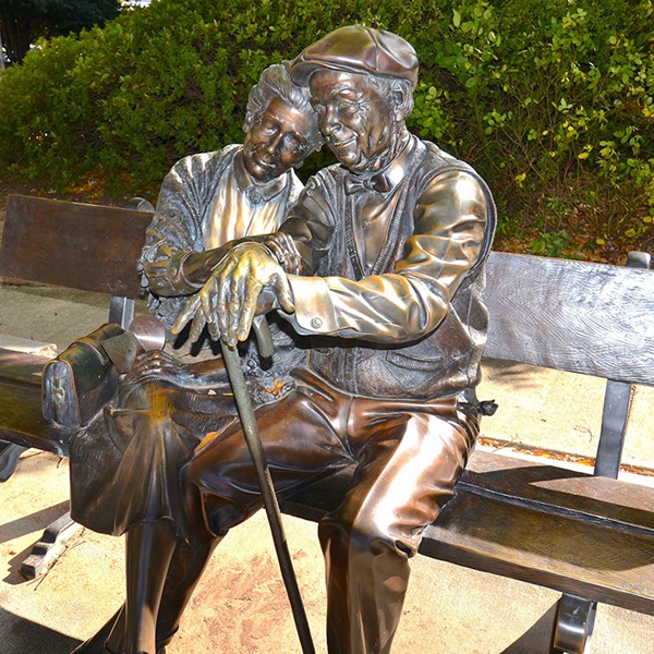 Bronze love old couple sculpture sitting on a bench in garden